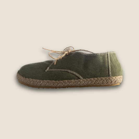 A single dark olive green suede slip-on shoe with a braided jute rope sole and matching rope laces, shown against a solid light beige background.