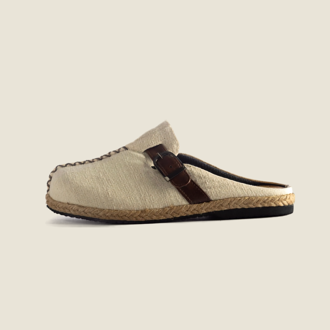 A single slip-on espadrille-style mule shoe in light beige woven fabric with a dark brown leather strap and braided jute sole, shown against a solid light beige background.