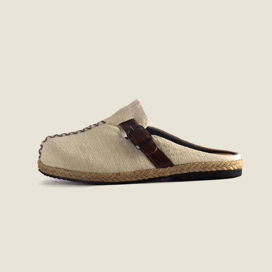 A single slip-on espadrille-style mule shoe in light beige woven fabric with a dark brown leather strap and braided jute sole, shown against a solid light beige background.